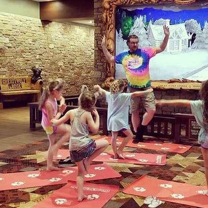 An instructor in a tie dye shirt leading children in yoga at Great Wolf Lodge.