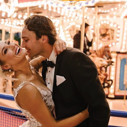 A husband and wife together in front of a carousel.